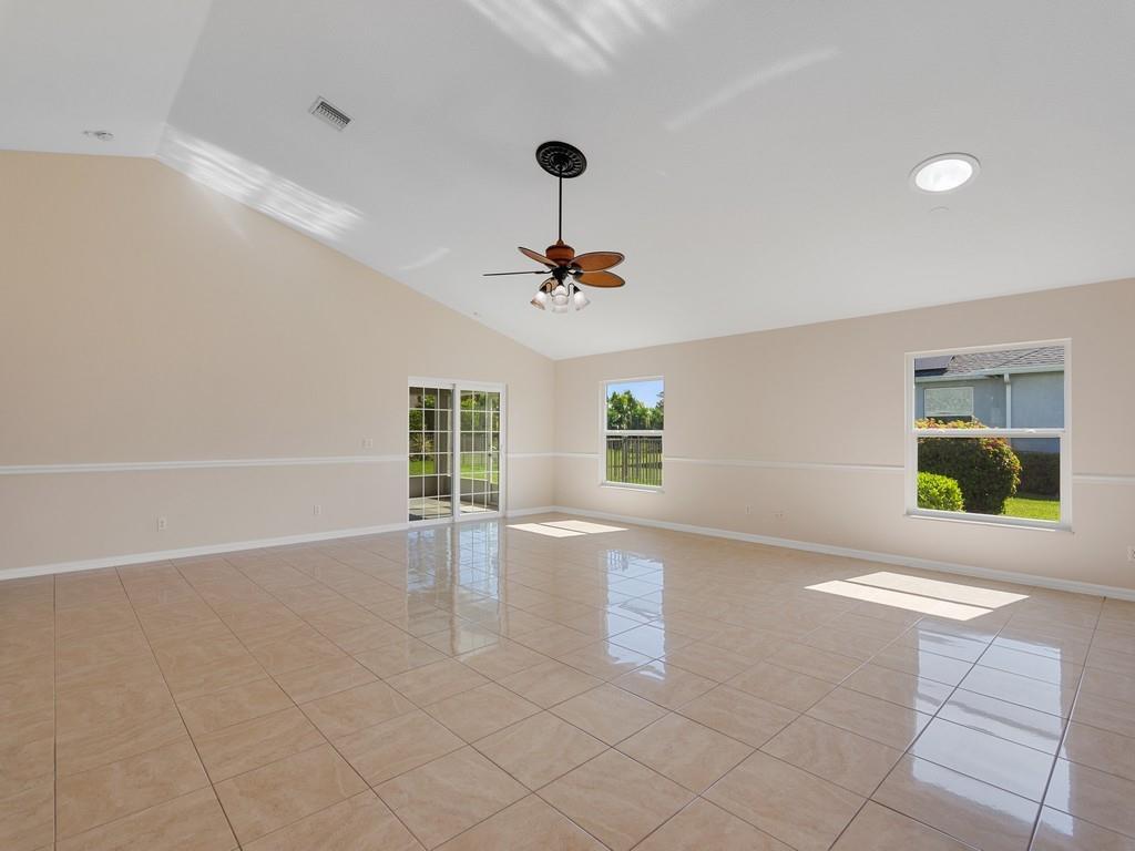 A spacious, empty room with vaulted ceilings, beige tile flooring, and large windows — 8340 Paladin Square, Vero Beach FL 32967, VERO BEACH, FL