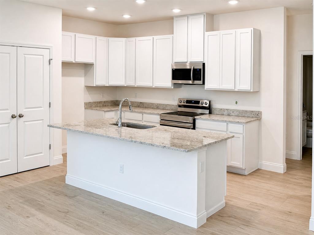 A kitchen features white cabinets, granite countertops, a center island, and stainless steel appliances — 808 SUNSHOWER DRIVE, LADY LAKE, FL