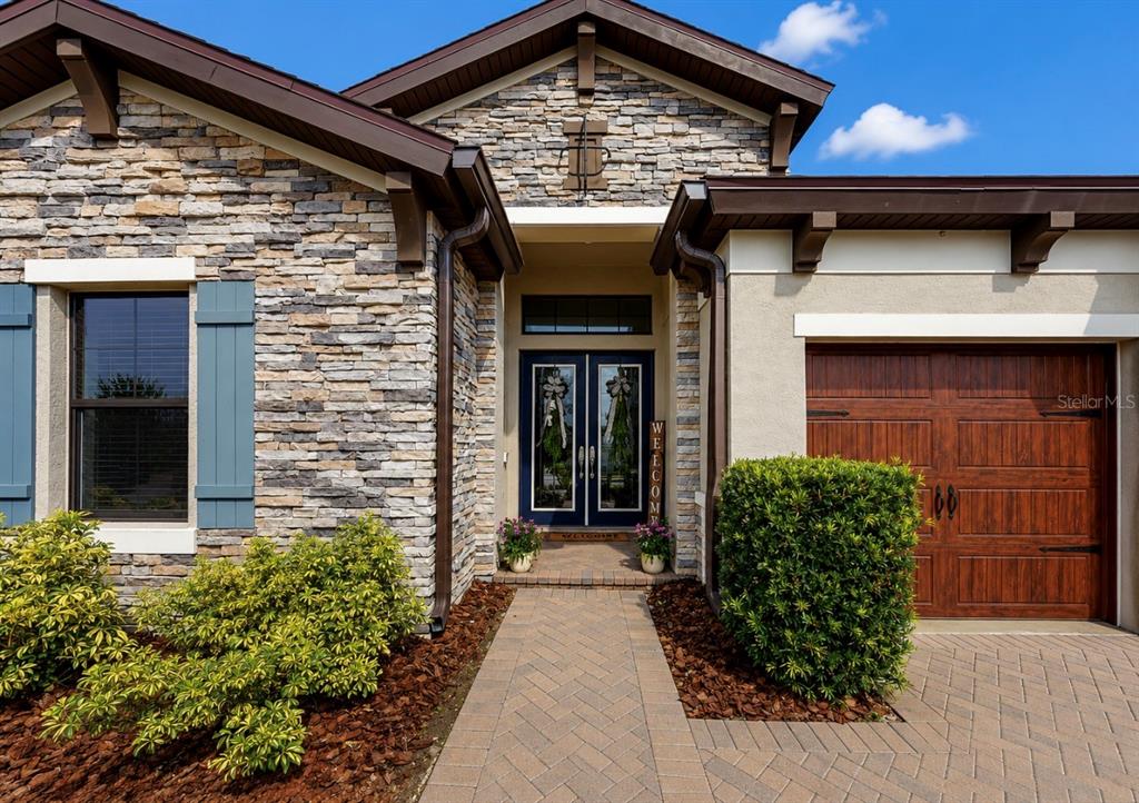 A stone-veneer house exterior features a double front door, a garage, and a paved walkway — 13211 WILDFLOWER MEADOW DRIVE, RIVERVIEW, FL