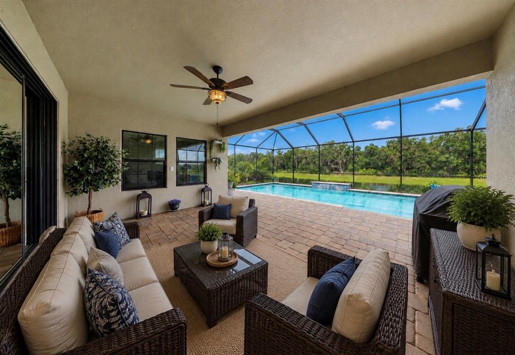 A covered patio features wicker furniture, a ceiling fan, and a screened-in pool overlooking greenery — 13211 WILDFLOWER MEADOW DRIVE, RIVERVIEW, FL