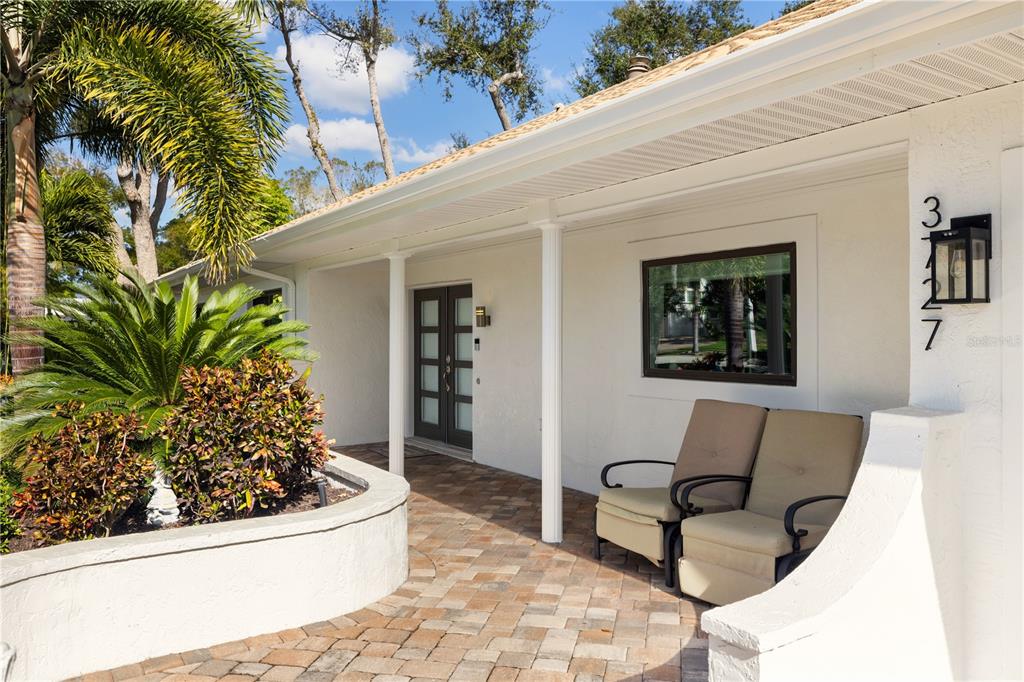 A paved porch features two tan chairs, a dark front door, and a white exterior — 3727 TANGIER TERRACE, SARASOTA, FL