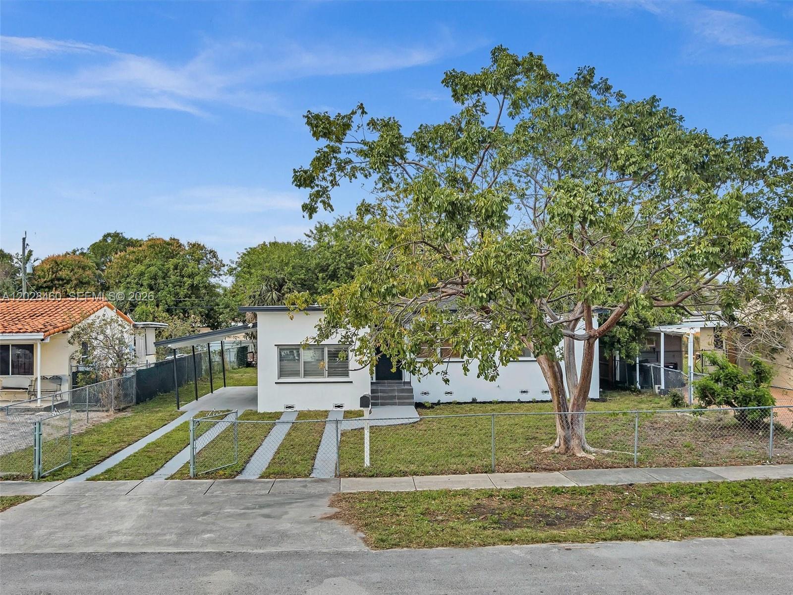 A white single-story house features a carport, a large tree, and a chain-link fence — 1365 NE 130th St, North Miami FL 33161, NORTH MIAMI, FL