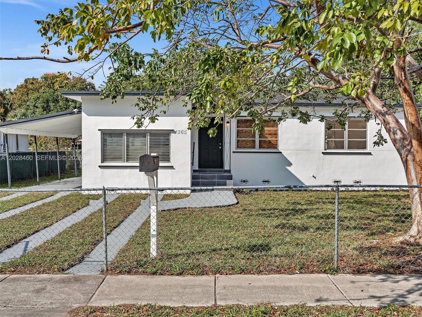 A white single-story house with a black front door and a chain-link fence — 1365 NE 130th St, North Miami FL 33161, NORTH MIAMI, FL