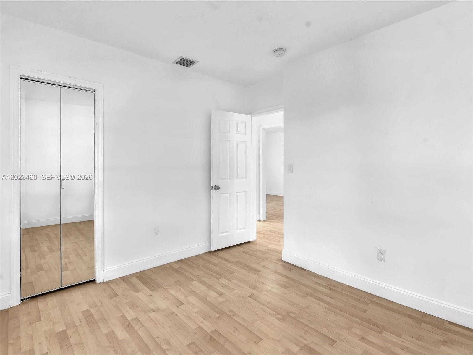 An empty room features light wood flooring, white walls, a mirrored closet, and an open door — 1365 NE 130th St, North Miami FL 33161, NORTH MIAMI, FL