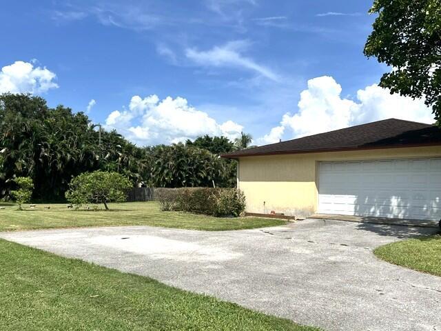 A yellow house with a white garage door sits next to a large grassy yard — 36911 3rd Street, Canal Point FL 33438, CANAL POINT, FL