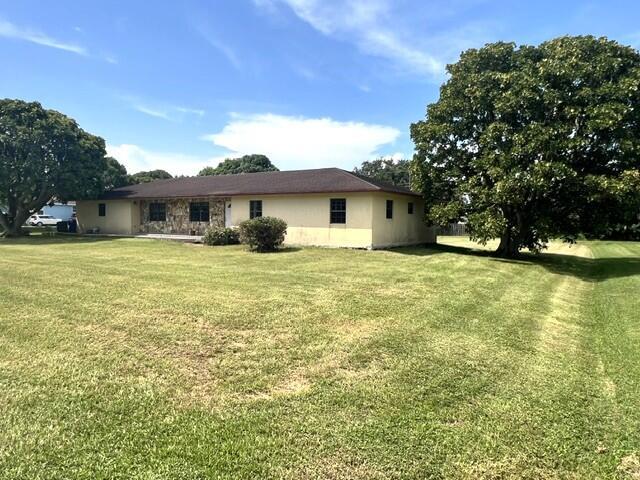 A single-story house with a stone facade and a large lawn under a blue sky — 36911 3rd Street, Canal Point FL 33438, CANAL POINT, FL