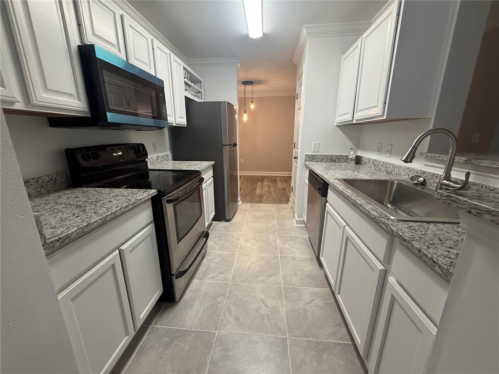 A galley kitchen features white cabinets, granite countertops, stainless steel appliances, and tile flooring — 18293 BRIDLE CLUB DRIVE UNIT 18293, TAMPA, FL