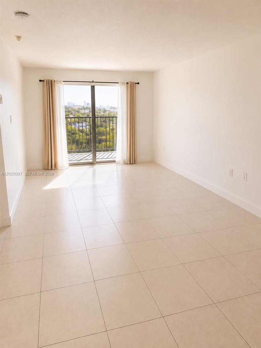 An empty room features light-colored tile flooring, white walls, and a sliding glass balcony door — 1975 Normandy Dr # 406, Miami Beach FL 33141, MIAMI BEACH, FL