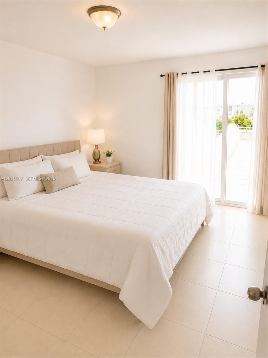 A bedroom features a bed with white bedding, a nightstand, and a sliding glass door — 1975 Normandy Dr # 406, Miami Beach FL 33141, MIAMI BEACH, FL