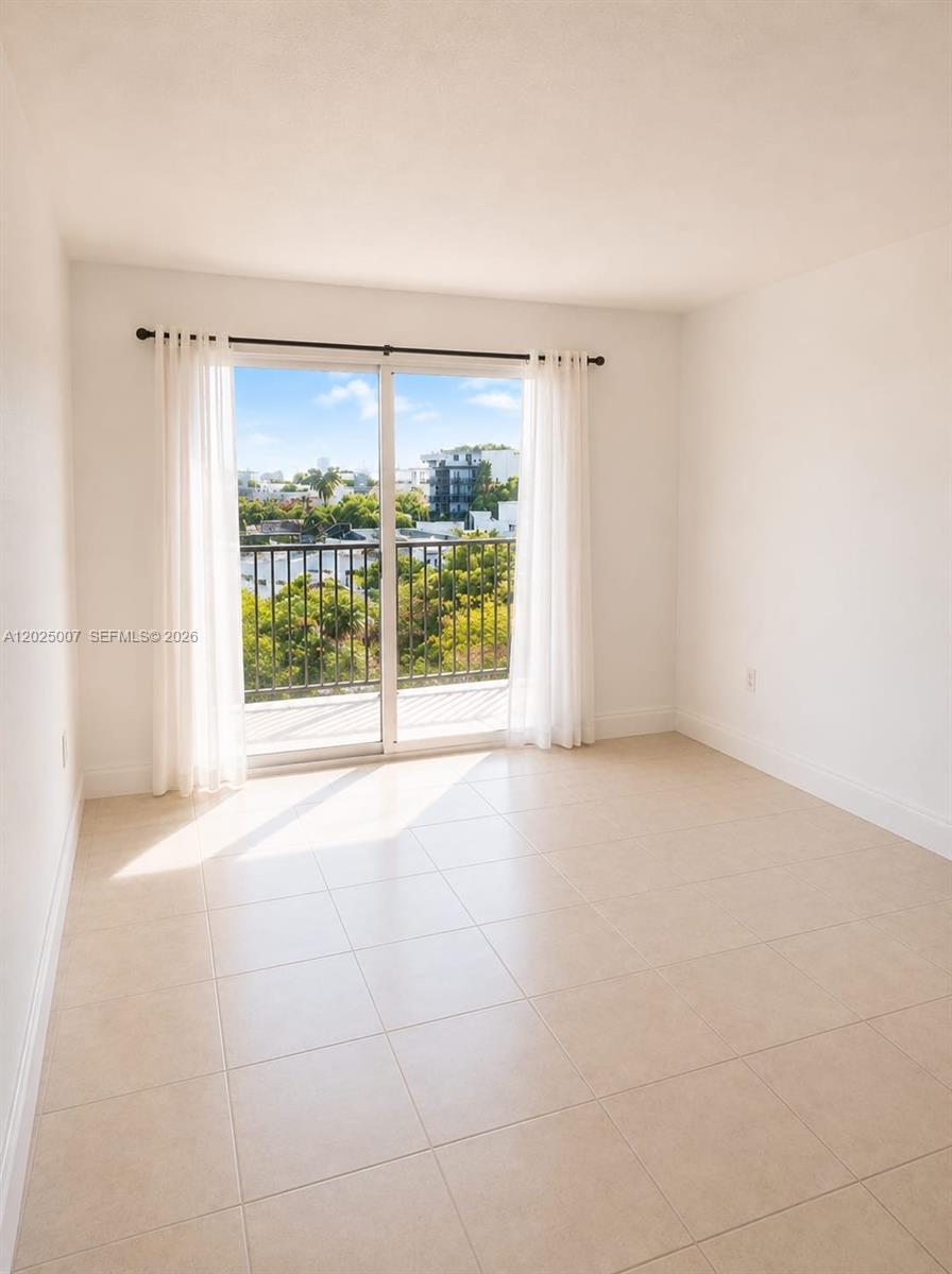An empty room with light-colored tile flooring features a sliding glass door leading to a balcony — 1975 Normandy Dr # 406, Miami Beach FL 33141, MIAMI BEACH, FL