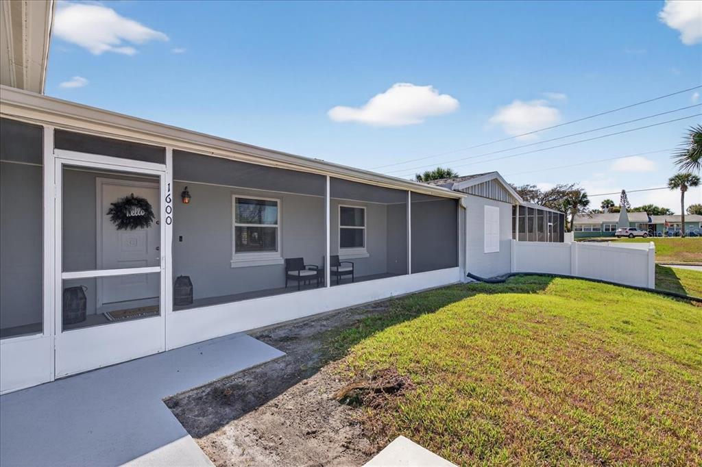 A screened-in front porch with a white door and gray siding on a sunny day — 1600 N OLEANDER AVENUE, DAYTONA BEACH, FL