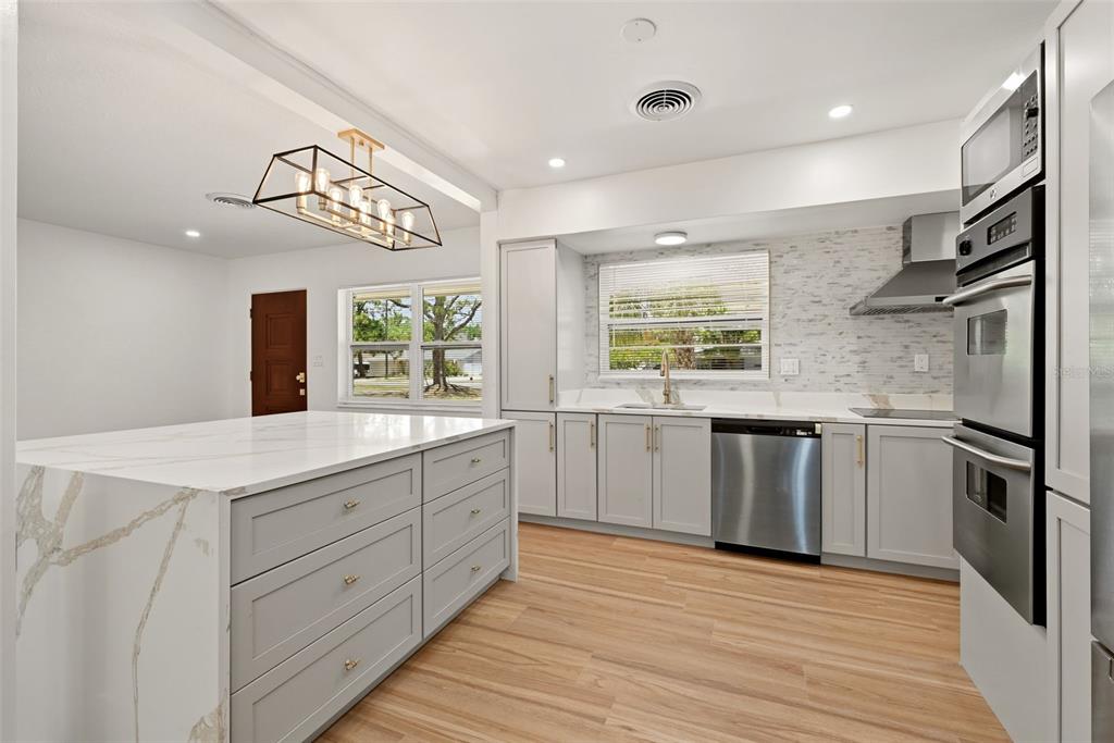 An open-concept living room and kitchen featuring light wood floors, white cabinetry, and an island — 2440 66TH AVENUE S, ST PETERSBURG, FL