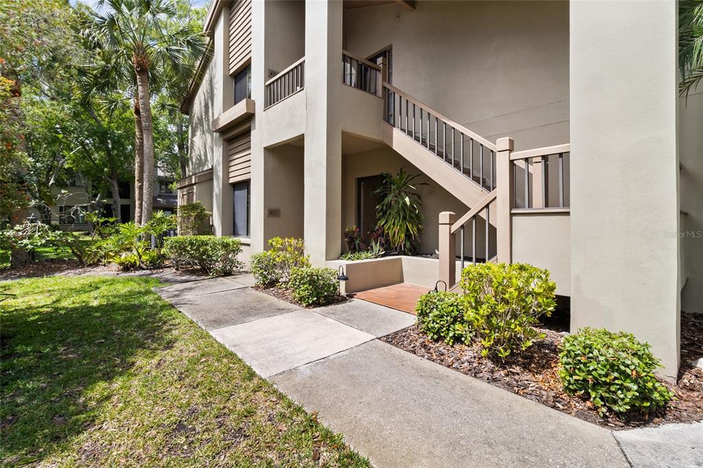 An exterior view of a multi-story apartment building with a concrete walkway and wooden stairs — 3016 LANDMARK BOULEVARD UNIT 401, PALM HARBOR, FL