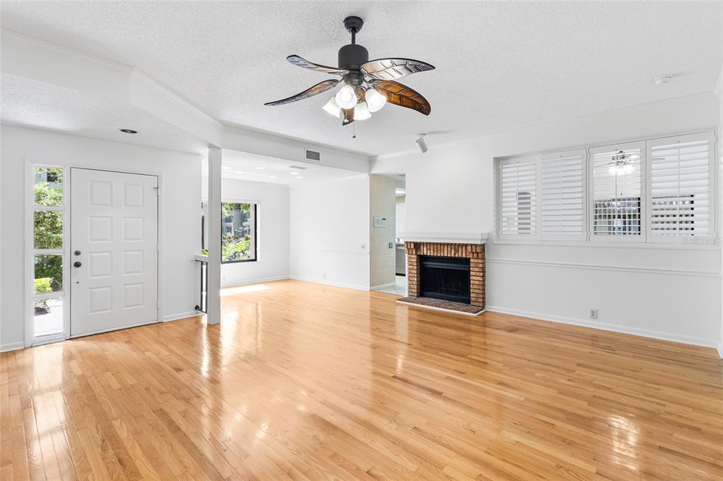 A bright living room features hardwood floors, a brick fireplace, and a ceiling fan — 3016 LANDMARK BOULEVARD UNIT 401, PALM HARBOR, FL