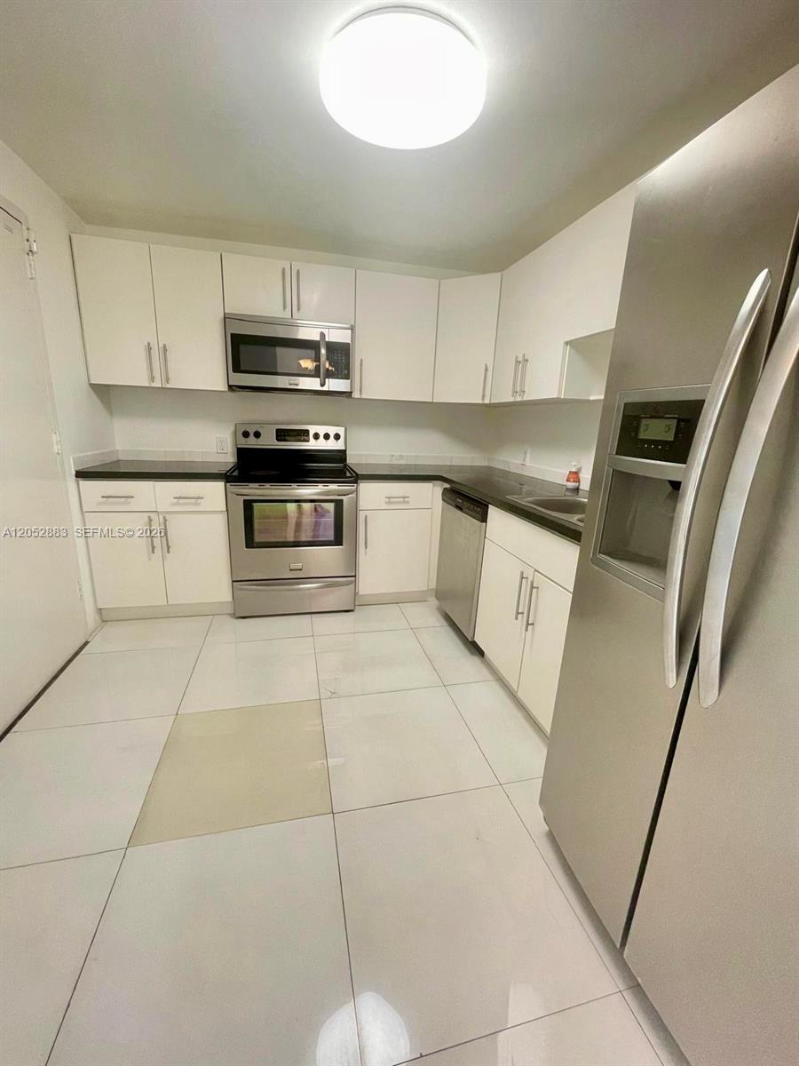 A kitchen features white cabinets, stainless steel appliances, and light-colored tile flooring — 13155 Ixora Ct # 201, North Miami FL 33181, NORTH MIAMI, FL