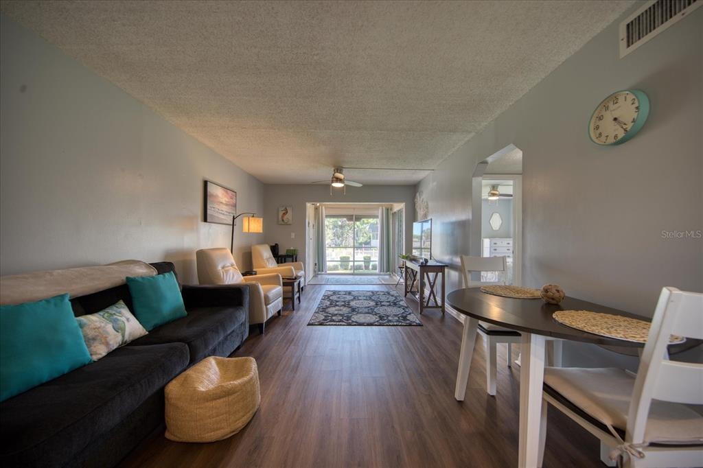 A living and dining area features wood-look flooring, a dark sofa, and a sliding glass door — 712 CORDOVA GREENS UNIT 712, SEMINOLE, FL