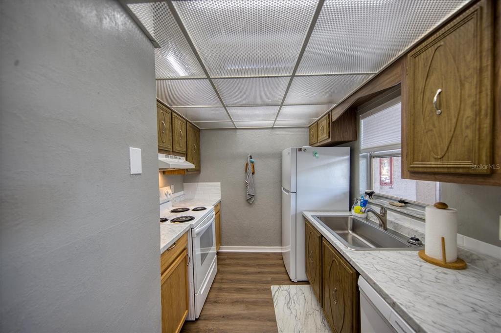A galley kitchen features wood cabinets, white appliances, marble-look countertops, and a drop ceiling — 712 CORDOVA GREENS UNIT 712, SEMINOLE, FL