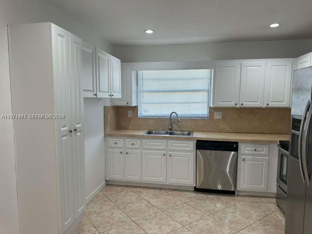 A kitchen features white cabinets, a stainless steel dishwasher, and light-colored tile flooring — 208 SW 2nd Ave, Hallandale Beach FL 33009, HALLANDALE BEACH, FL