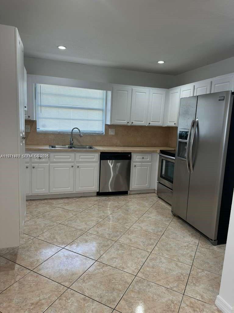 A kitchen features white cabinets, stainless steel appliances, and light-colored tile flooring — 208 SW 2nd Ave, Hallandale Beach FL 33009, HALLANDALE BEACH, FL