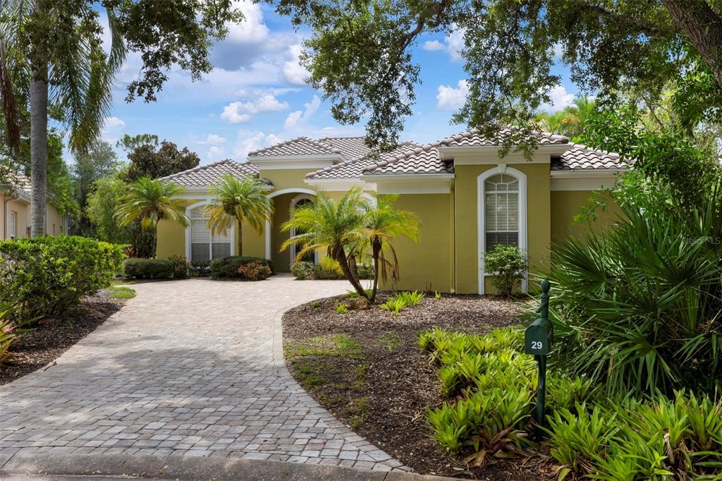 A single-story house with a paved driveway, green stucco exterior, and lush landscaping — 29 SAINT JOHN BOULEVARD UNIT 5, ENGLEWOOD, FL