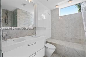A modern bathroom features a white double vanity, marble walls, and a walk-in shower — 1600 Michigan Ave # 7, Miami Beach FL 33139, MIAMI BEACH, FL