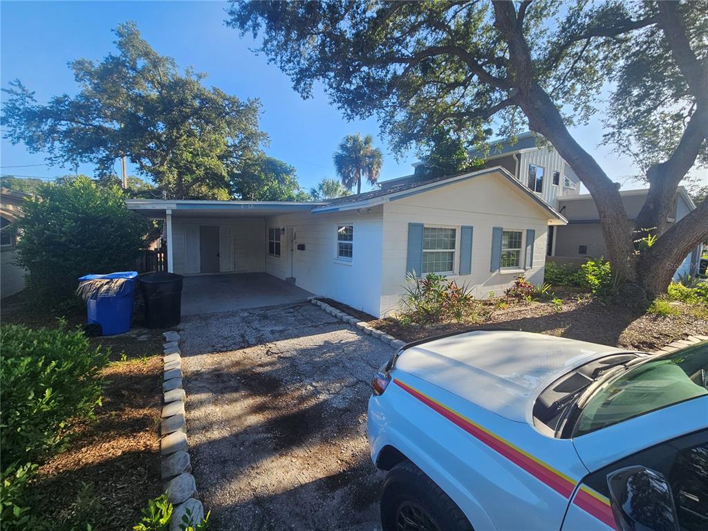 A single-story house with a carport, a gravel driveway, and blue shutters under large trees — 8068 23RD AVENUE N, ST PETERSBURG, FL