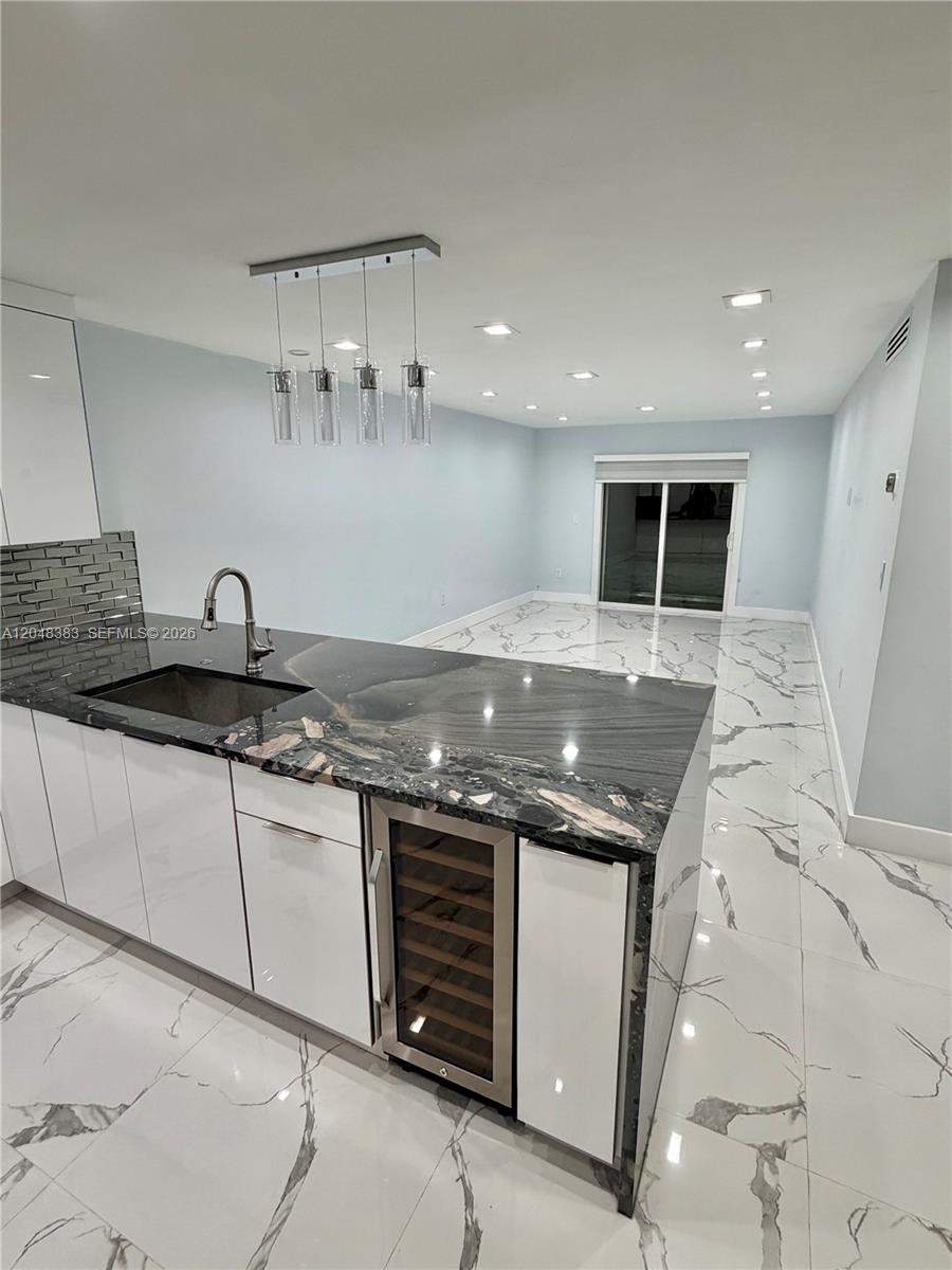 A modern kitchen features a black granite island with a wine cooler and white cabinets — 1100 W 35th St # 4, Hialeah FL 33012, HIALEAH, FL