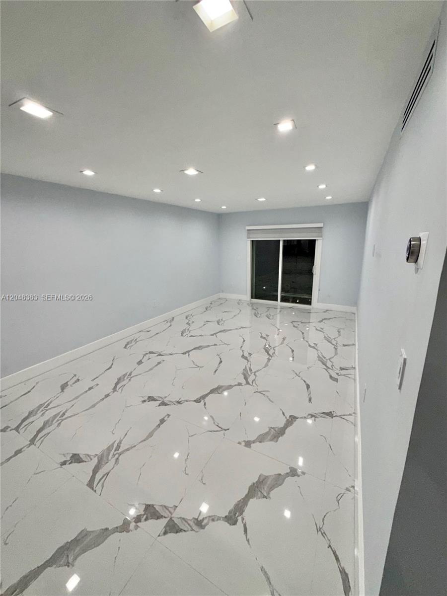 An empty room features light blue walls, recessed lighting, and white marble-patterned tile flooring — 1100 W 35th St # 4, Hialeah FL 33012, HIALEAH, FL