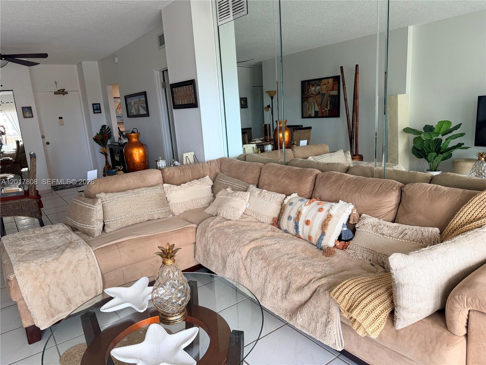 A living room features a large tan sectional sofa, a glass coffee table, and mirrored walls — 1950 S Ocean Dr # 4B, Hallandale Beach FL 33009, HALLANDALE BEACH, FL