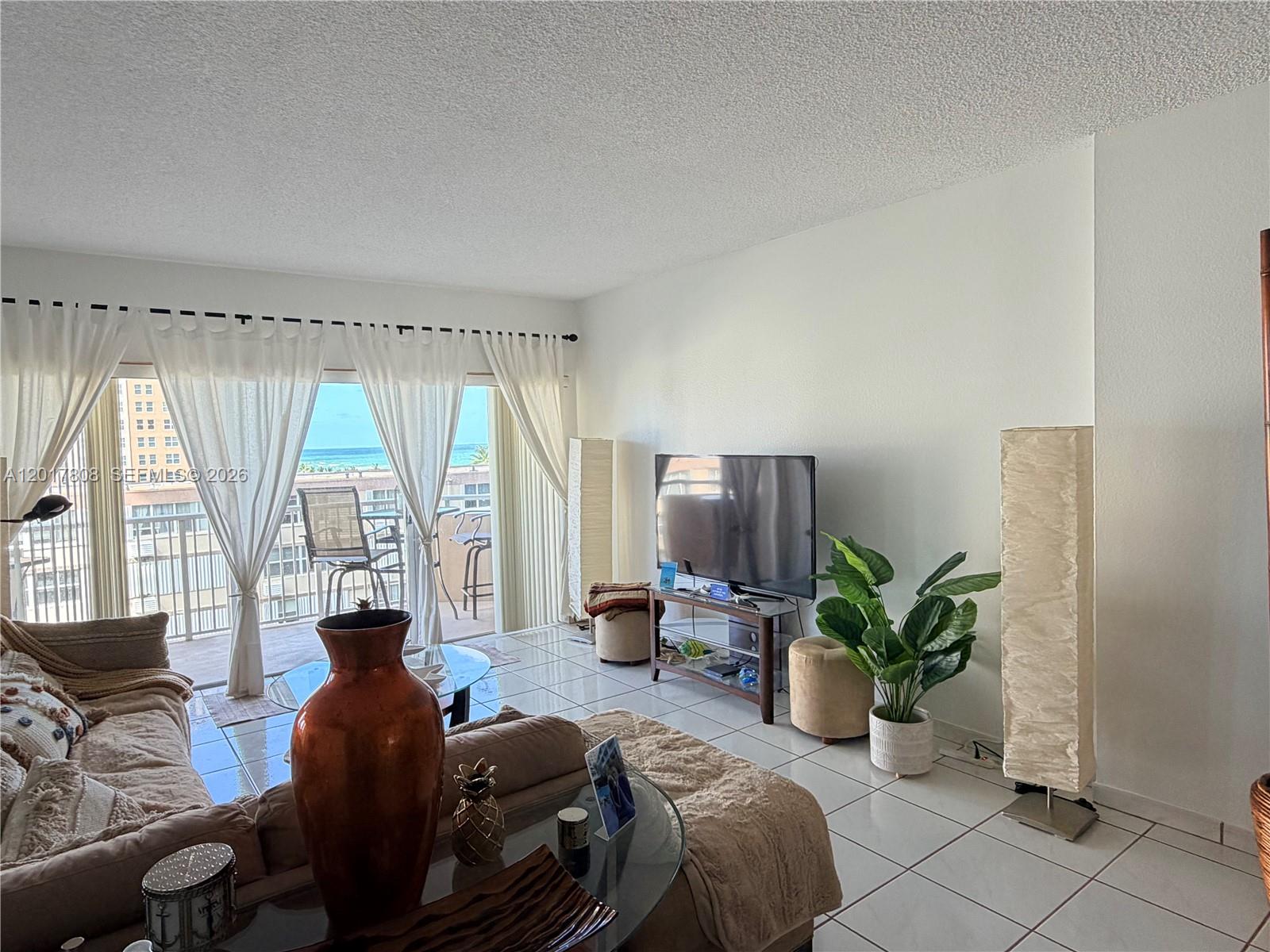A living room with tile floors, a television, and a balcony overlooking the ocean — 1950 S Ocean Dr # 4B, Hallandale Beach FL 33009, HALLANDALE BEACH, FL