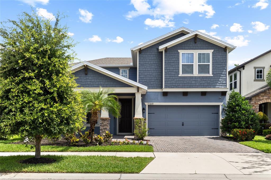 A two-story blue house features a two-car garage, stone accents, and a front palm tree — 11641 SWEET TANGERINE LANE, TAMPA, FL