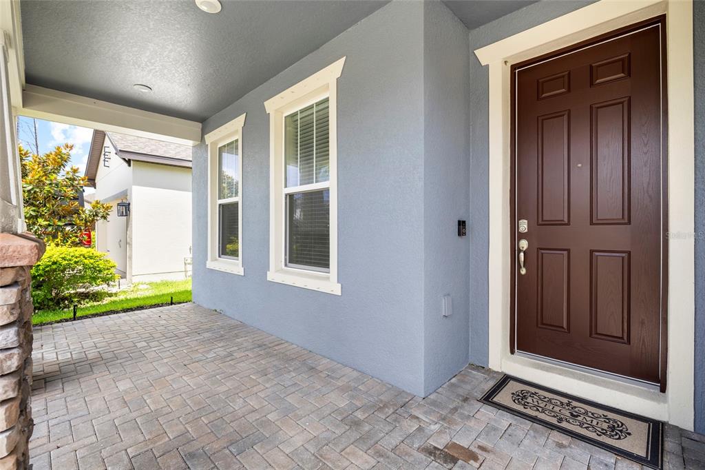 A covered porch with brick pavers leads to a brown front door on a house — 11641 SWEET TANGERINE LANE, TAMPA, FL