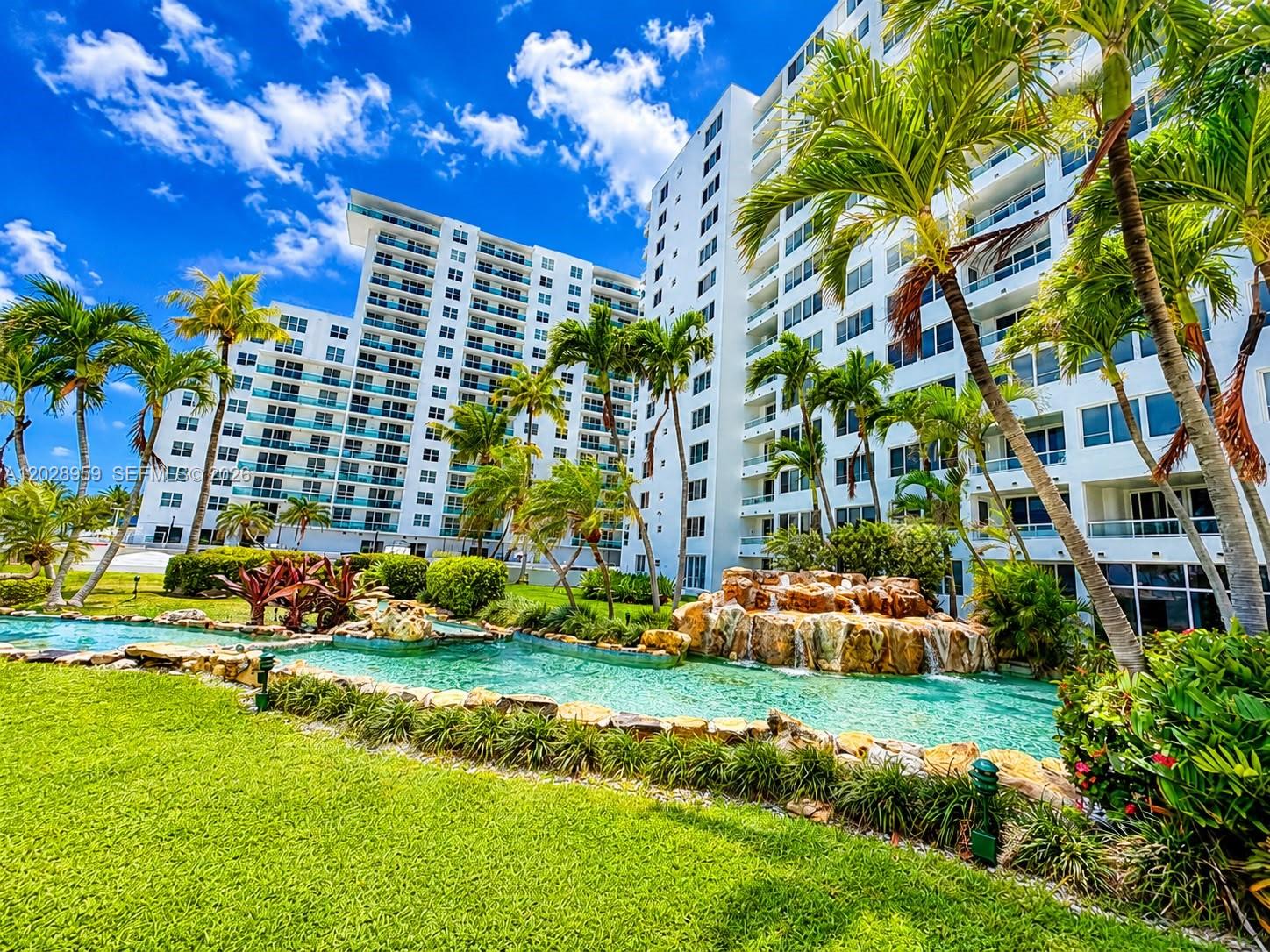 A multi-story white apartment building overlooks a landscaped pool area with a rock waterfall — 5005 Collins Ave # 616, Miami Beach FL 33140, MIAMI BEACH, FL