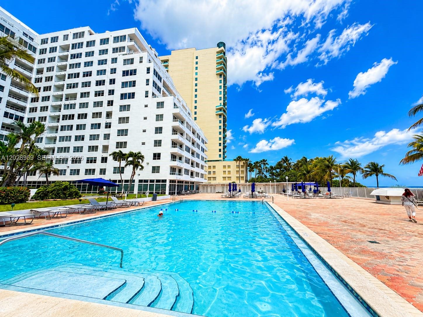 A large swimming pool sits on a paved deck in front of a tall apartment building — 5005 Collins Ave # 616, Miami Beach FL 33140, MIAMI BEACH, FL