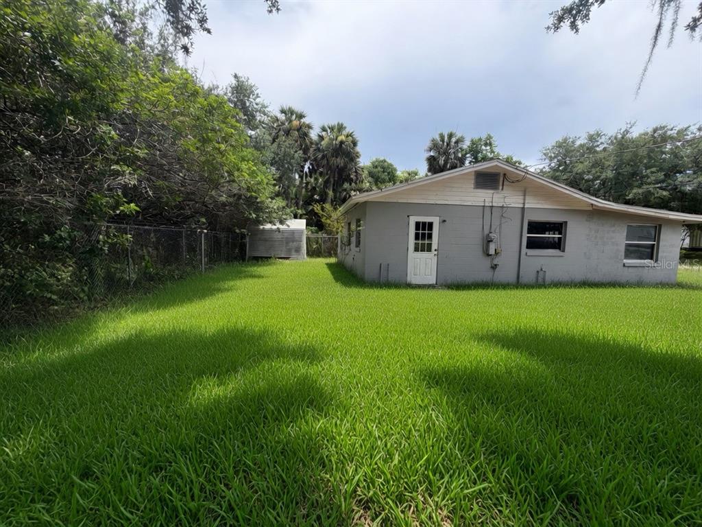 A gray house with a white door sits beside a large, grassy backyard — 3312 W 5TH STREET, SANFORD, FL