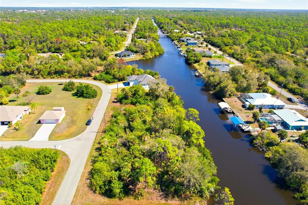 An aerial view shows a residential canal with houses, docks, and surrounding wooded areas — 594 MCDILL DRIVE, PORT CHARLOTTE, FL