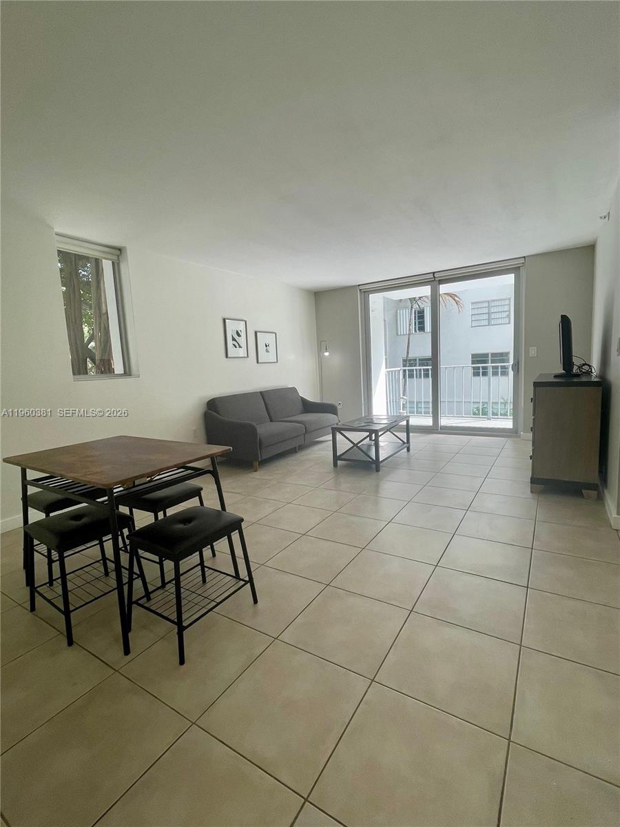 This living and dining area features tile flooring, a grey sofa, and a sliding glass door — 700 NE 63rd St # D203, Miami FL 33138, MIAMI, FL