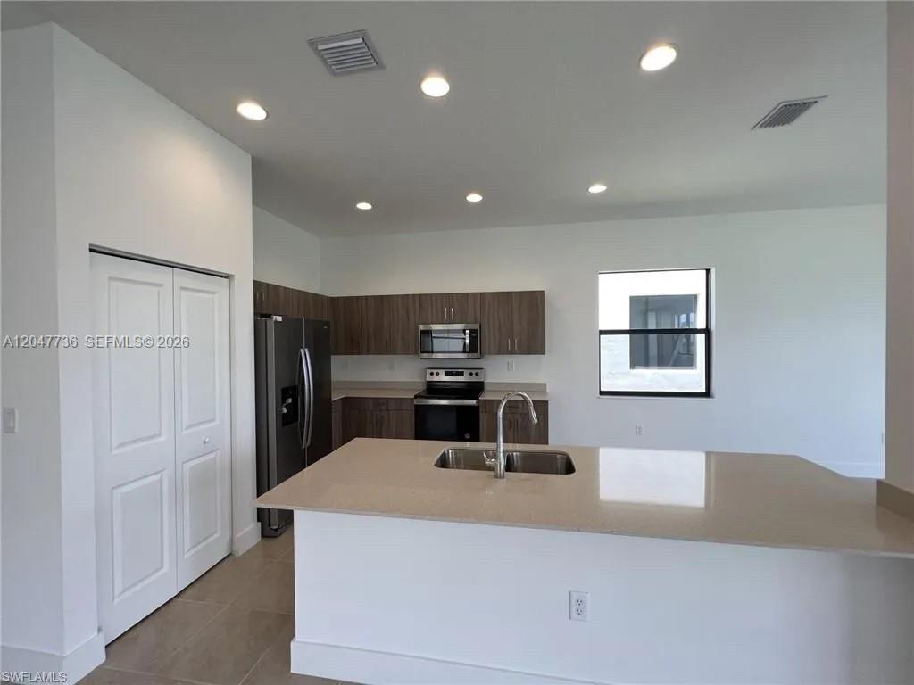 A kitchen features a central island with a sink, stainless steel appliances, and wood cabinetry — 5645 Cerva Lane # 5645, Ave Maria FL 34142, AVE MARIA, FL