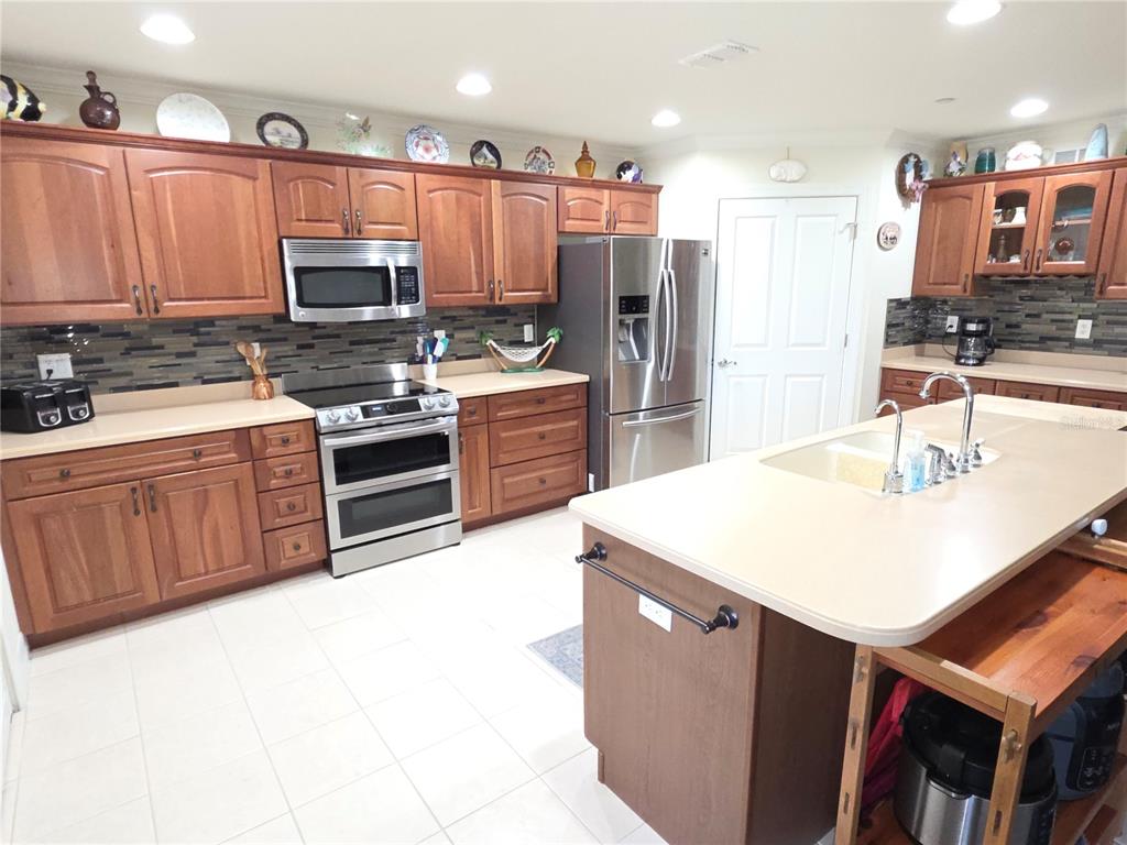 A kitchen features wood cabinets, stainless steel appliances, a center island, and a tiled backsplash — 8152 SOUTHERN PINES DRIVE, BROOKSVILLE, FL