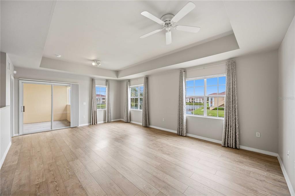 An empty living room features light wood-look flooring, a tray ceiling, and a sliding glass door — 1025 VILLAGIO CIRCLE UNIT 208, SARASOTA, FL