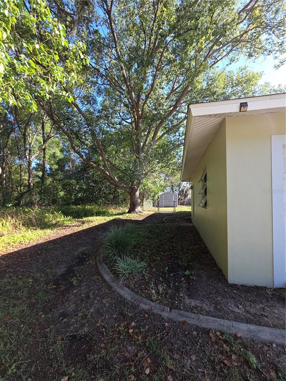 A side view of a house exterior with a curved garden bed and large trees — 9091 N GOLFVIEW DRIVE, CITRUS SPRINGS, FL