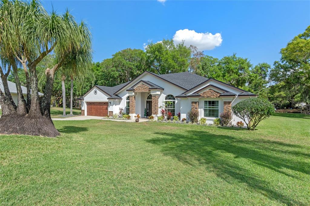 A single-story house with a white exterior, stone accents, and a large front lawn — 11516 LYONS COURT, CLERMONT, FL