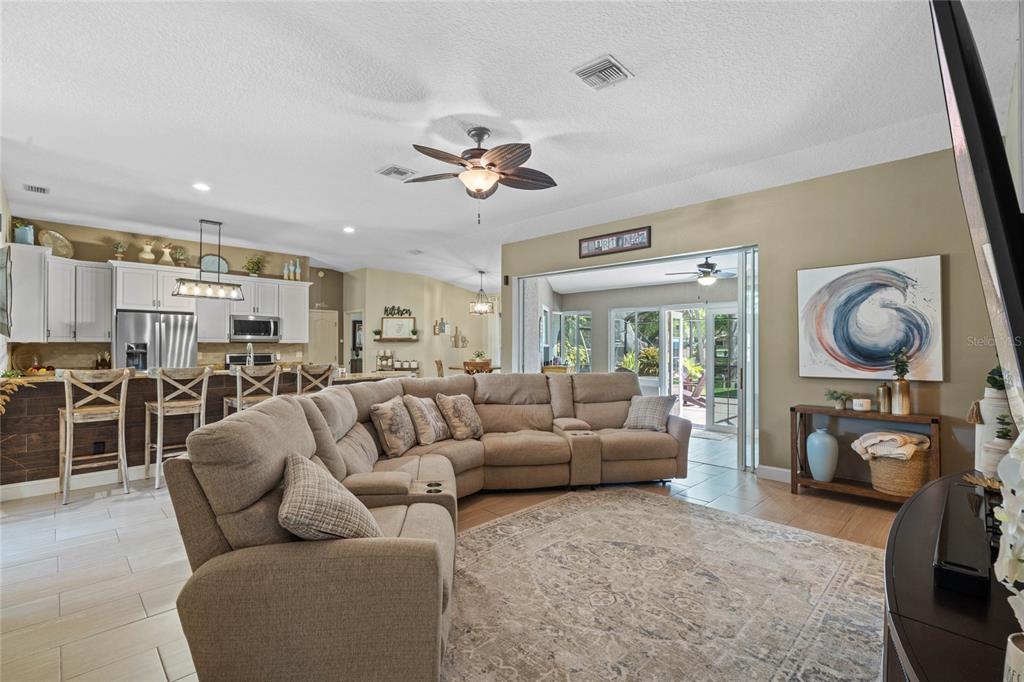 A living room with a large sectional sofa, tile floors, and an open kitchen area — 11516 LYONS COURT, CLERMONT, FL