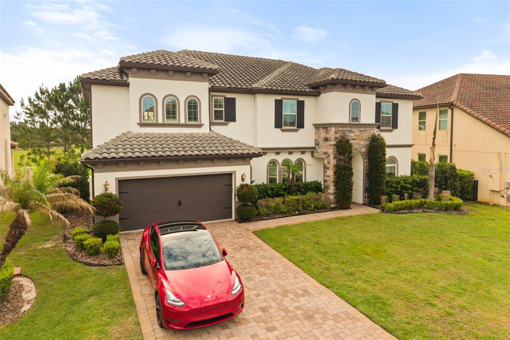 A two-story house with a stone-accented entrance, a three-car garage, and a red car parked — 8507 GEDDES LOOP, ORLANDO, FL