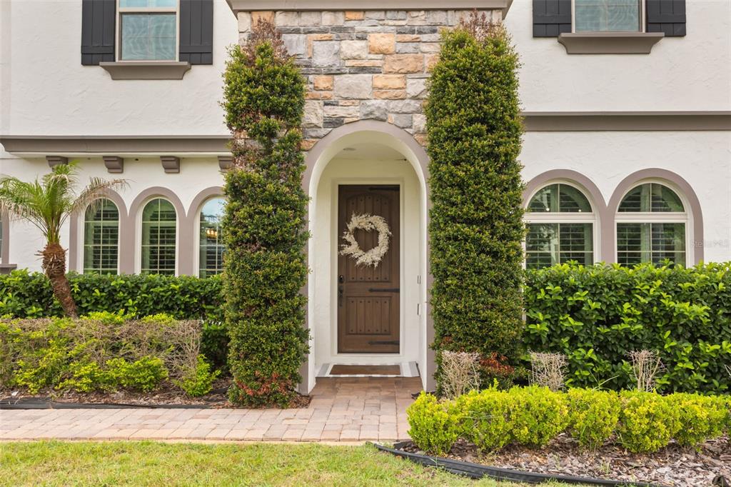 The exterior of a house features a stone-accented arched entryway, a wooden door, and landscaping — 8507 GEDDES LOOP, ORLANDO, FL