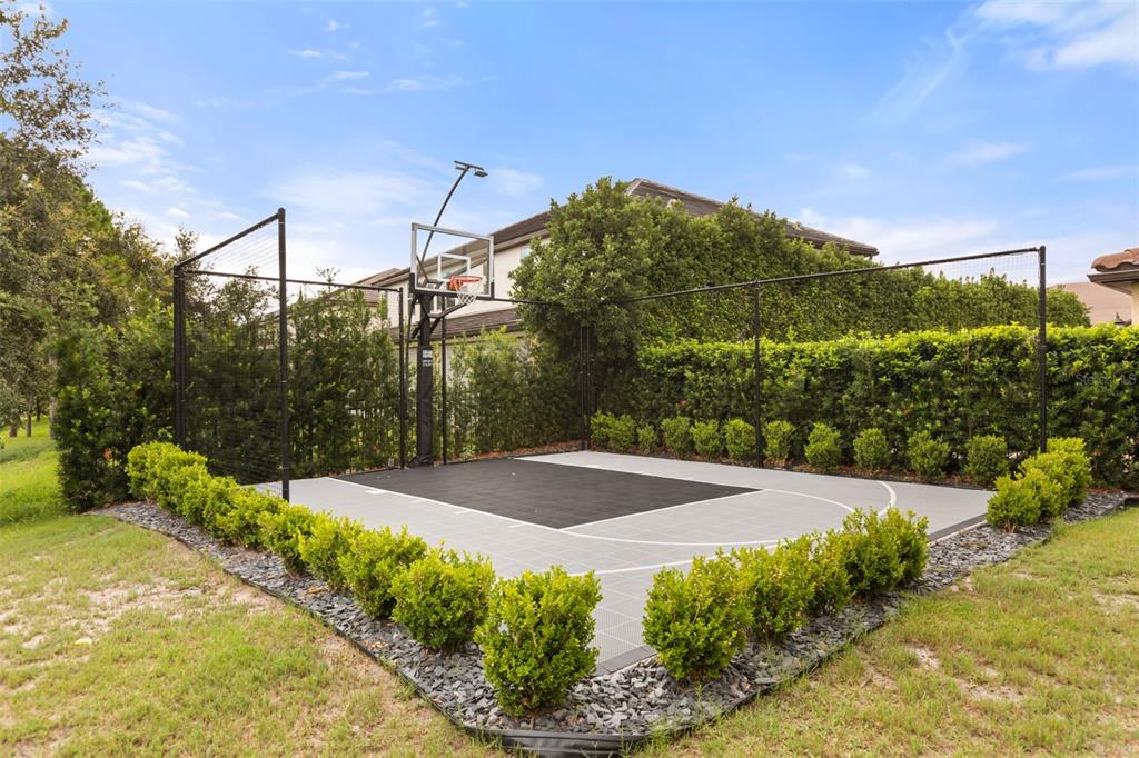 An outdoor basketball court with a hoop and black netting is surrounded by manicured hedges — 8507 GEDDES LOOP, ORLANDO, FL