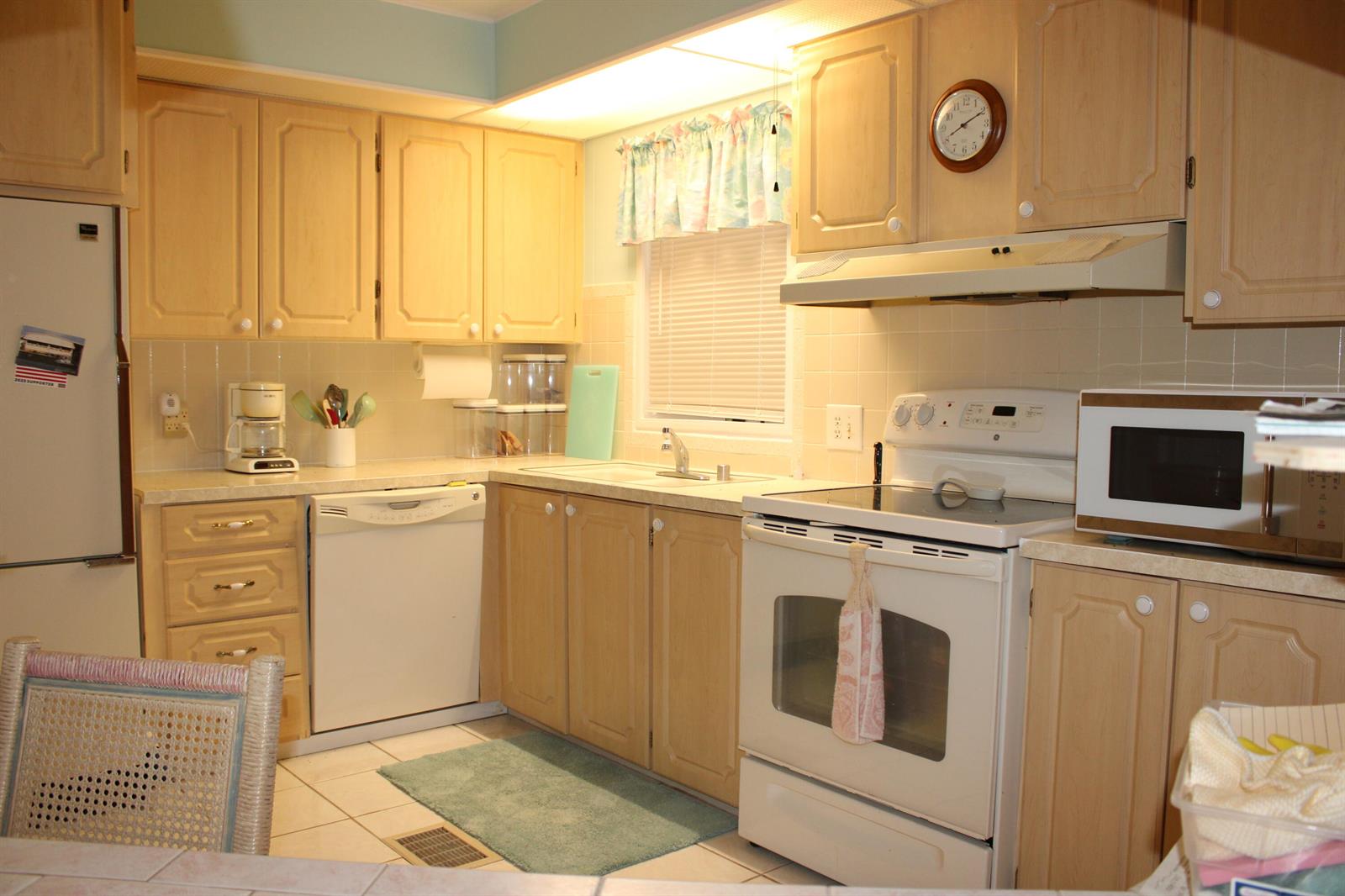 A kitchen features light wood cabinets, white appliances, tiled countertops, and a window with a valance — 37010 Exuma Bay, Boynton Beach FL 33436, BOYNTON BEACH, FL