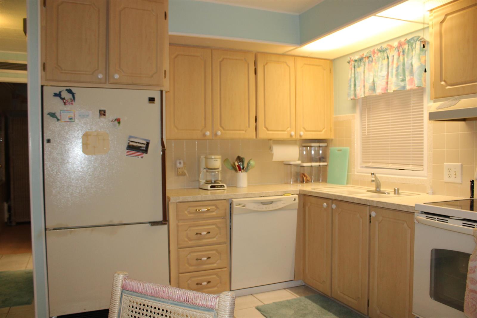 A kitchen features light wood cabinets, white appliances, a tiled backsplash, and a window with curtains — 37010 Exuma Bay, Boynton Beach FL 33436, BOYNTON BEACH, FL