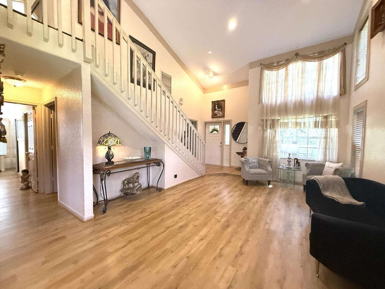 A living room features light wood flooring, a staircase with white railings, and tall windows — 14765 Northlake Boulevard, FL 33412, FL