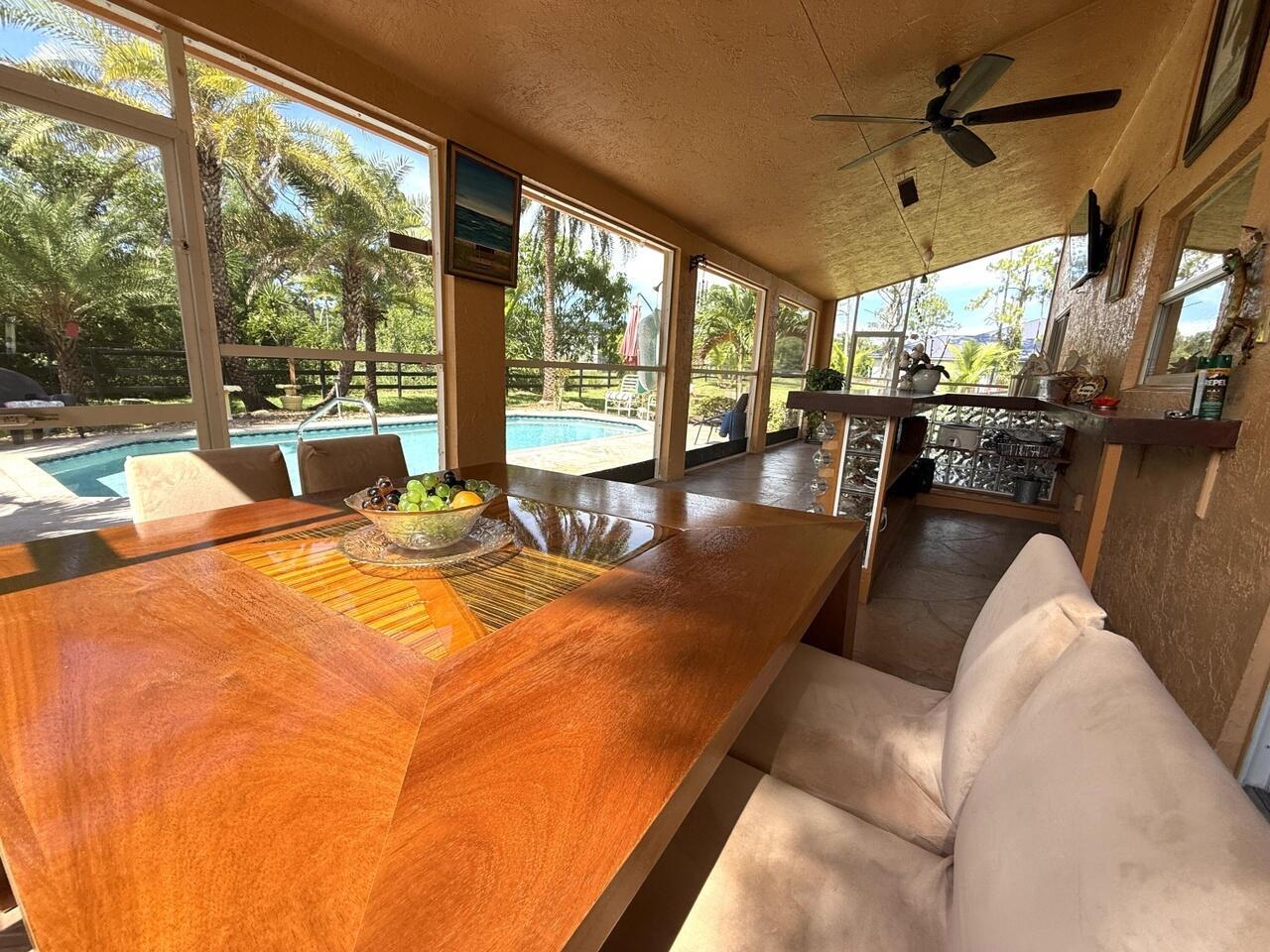 A screened-in patio features a wooden dining table, a built-in bar, and a swimming pool — 14765 Northlake Boulevard, FL 33412, FL